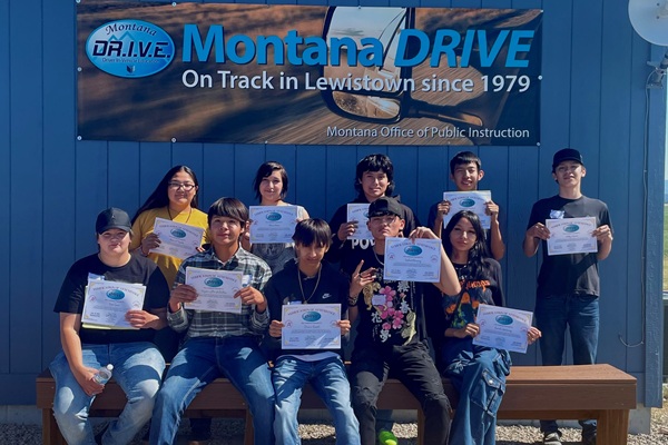 Teens sitting at a table holding certificates