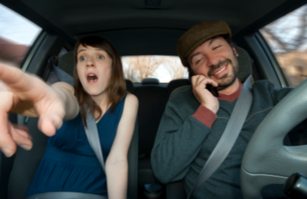 Woman in car pointing while driver is on his phone