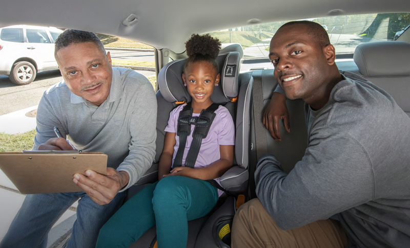 A child in a car seat in the back seat of a car with an adult on either side