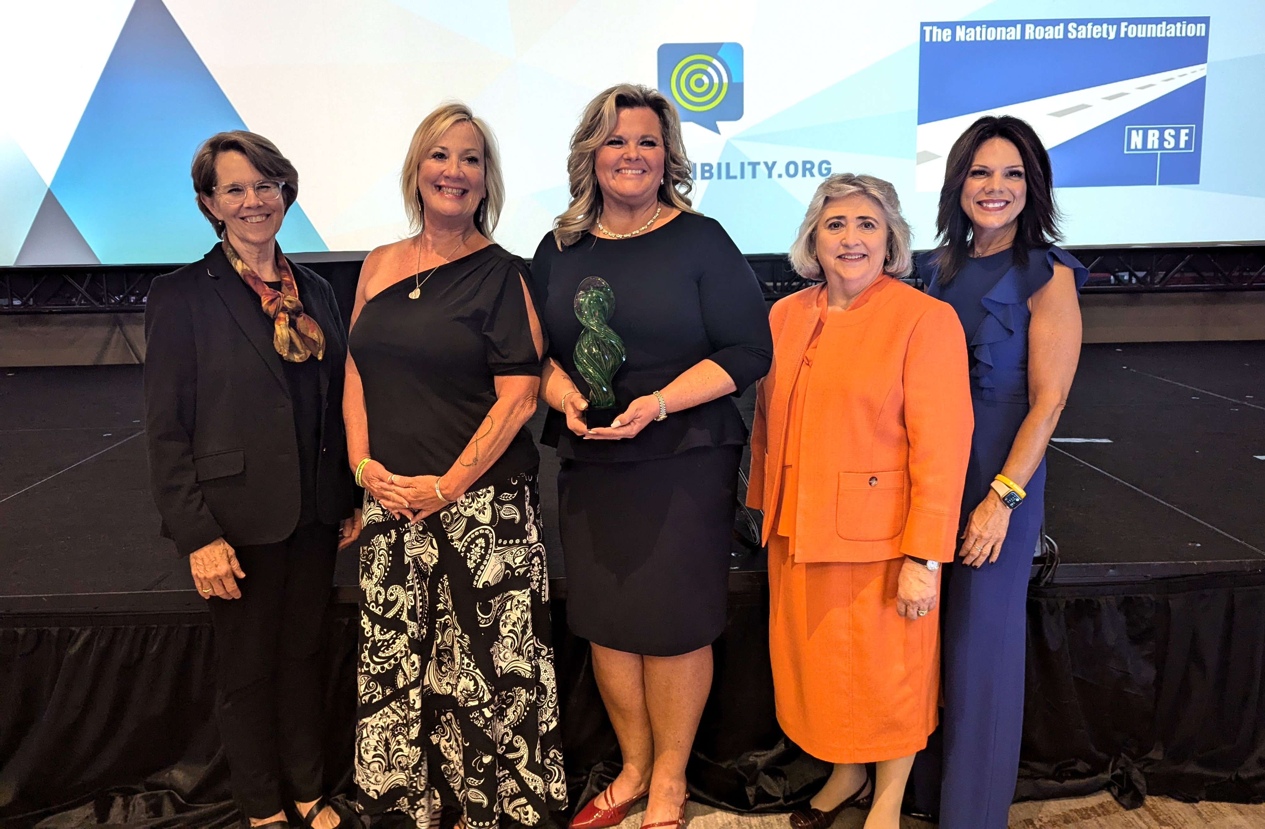 Five women standing together holding a glass award